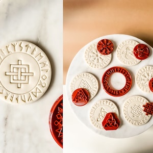 Puede incluir: Un conjunto de ocho sellos de goma roja con varios símbolos y runas vikingos. Los sellos están dispuestos sobre una superficie blanca con círculos de masa blanca que han sido sellados con los diseños.