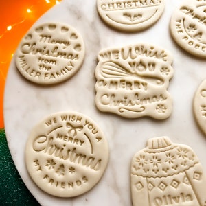 May include: Assortment of six white sugar cookies decorated with Christmas-themed designs. The cookies feature phrases like "We Wish You a Merry Christmas", "Merry Christmas from the Miller Family", and "Merry Christmas My Friends".