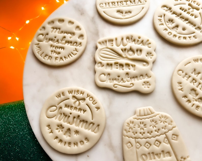 May include: Assortment of six white sugar cookies decorated with Christmas-themed designs. The cookies feature phrases like "We Wish You a Merry Christmas", "Merry Christmas from the Miller Family", and "Merry Christmas My Friends".