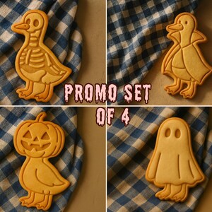 May include: A set of four Halloween-themed cookies. The cookies are shaped like a duck skeleton, a duck in a cape, a jack-o'-lantern, and a ghost. The cookies are light brown and sit on a blue and white checkered cloth. The text "PROMO SET OF 4" is visible.