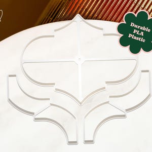 May include: A white, geometric design made of durable PLA plastic. The design features a symmetrical pattern with curved and angular elements. The text "Durable PLA Plastic" is displayed on a green flower-shaped graphic. The logo "lek lek" is in the upper left corner.