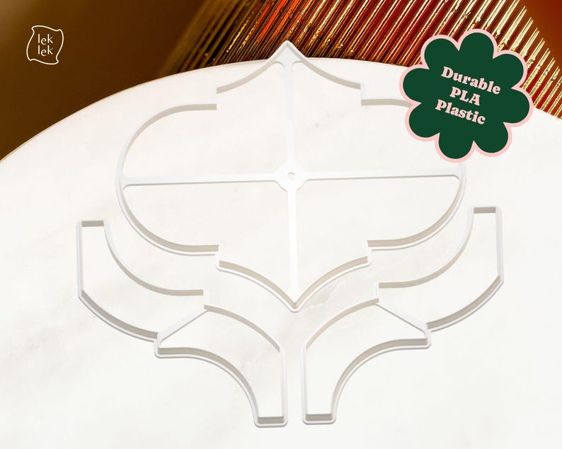 May include: A white, geometric design made of durable PLA plastic. The design features a symmetrical pattern with curved and angular elements. The text "Durable PLA Plastic" is displayed on a green flower-shaped graphic. The logo "lek lek" is in the upper left corner.