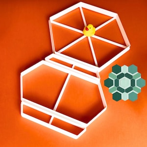 May include: White geometric container with an open lid, featuring a yellow rubber duck. A green and blue geometric design is next to the container, all on an orange surface.