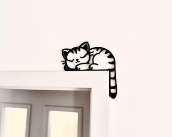 May include: Black and white silhouette of a sleeping cat with its tail hanging down. The cat is positioned on a white door frame.