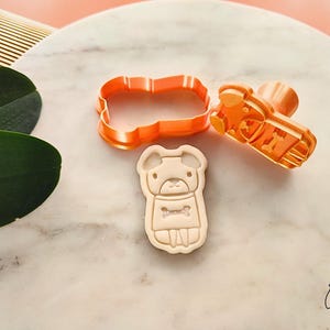 Puede incluir: Un juego de cortador y sello de galletas con forma de perro de pl&aacute;stico naranja. El juego incluye un cortador, un sello y una galleta con un dise&ntilde;o de perro y un hueso. El cortador mide aproximadamente 7,6 cm de largo.