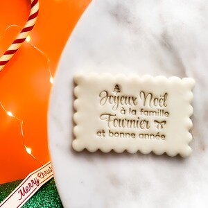 May include: A white cookie with a scalloped edge and a message in French that reads "Joyeux Noel a la famille Fournier et bonne année" which translates to "Merry Christmas to the Fournier family and a Happy New Year".