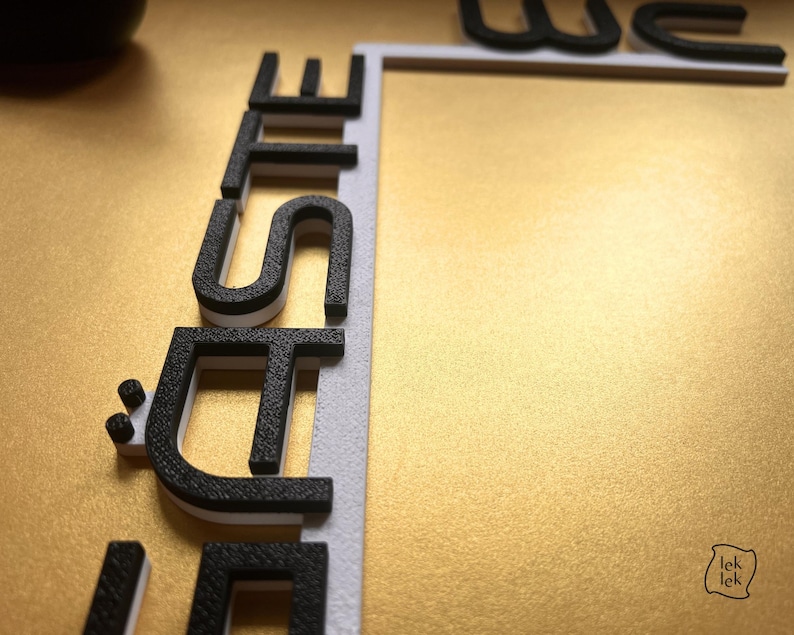May include: Close-up of a gold surface with the word "SITE" in black and white 3D letters. The letters are positioned vertically along a white border. The word "WE" is partially visible at the top. The image has a textured gold background.