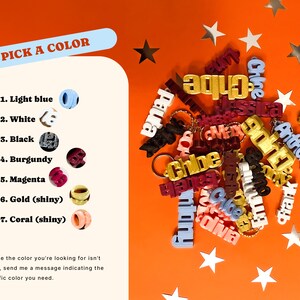 May include: A variety of personalized keychains in different colors, including light blue, white, black, burgundy, magenta, gold, and coral. The keychains are made of plastic and have a shiny finish. The keychains are arranged on a bright orange background with silver stars.