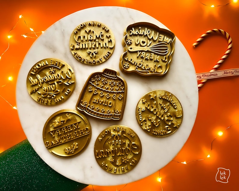 May include: Set of 7 gold-colored cookie cutters with Christmas-themed designs. The designs include "We Wish You A Merry Christmas", "Oh The Wonderful Time Of The Year", "Merry Christmas", "It's The Most Wonderful Time Of The Year", "Jingle All The Way", "Have Yourself A Merry Little Christmas", and a sweater.