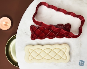 May include: Red plastic cookie cutters in the shape of a braided design. A cookie is shown with the braided design imprinted on it.