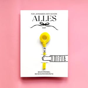 以下が含まれることがあります： ドイツ語のテキストと黄色のふわふわしたクリーニングブラシが描かれた白いカード。カードには「F&Uuml;R JEMANDEN DER SCHON ALLES HAT」と「BAUCHNABEL REINIGUNGSB&Uuml;RSTE」と書かれています。ブラシには数字の「40」が書かれています。