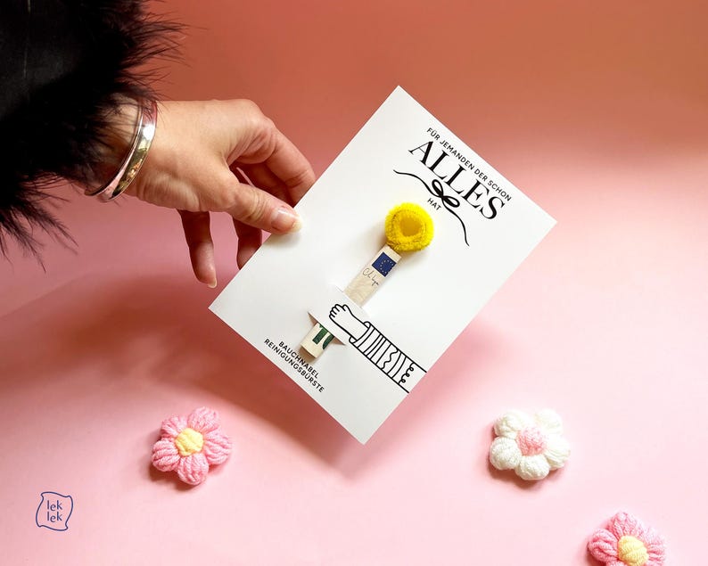 May include: A white rectangular card featuring a small wooden cleaning brush with a yellow fuzzy tip. The card displays the text "F&Uuml;R JEMANDEN DER SCHON ALLES HAT" and "BAUCHNABEL REINIGUNGSB&Uuml;RSTE" alongside a black line drawing of a hand and arm.