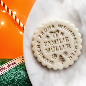 May include: A white cookie with a brown imprint that reads "Frohe Weihnachten w&uuml;nscht Familie M&uuml;ller".