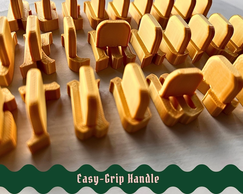 May include: A collection of gold-colored, 3D-printed plastic components, each featuring a vertical tab and a base, arranged in rows. The text "Easy-Grip Handle" is displayed in a dark green, wavy-edged banner at the bottom of the image.