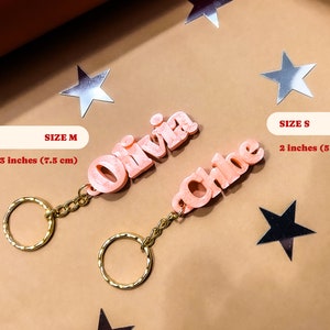 May include: Two pink personalized keychains with the names Olivia and Chloe. The Olivia keychain is 3 inches (7.5 cm) and the Chloe keychain is 2 inches (5 cm).