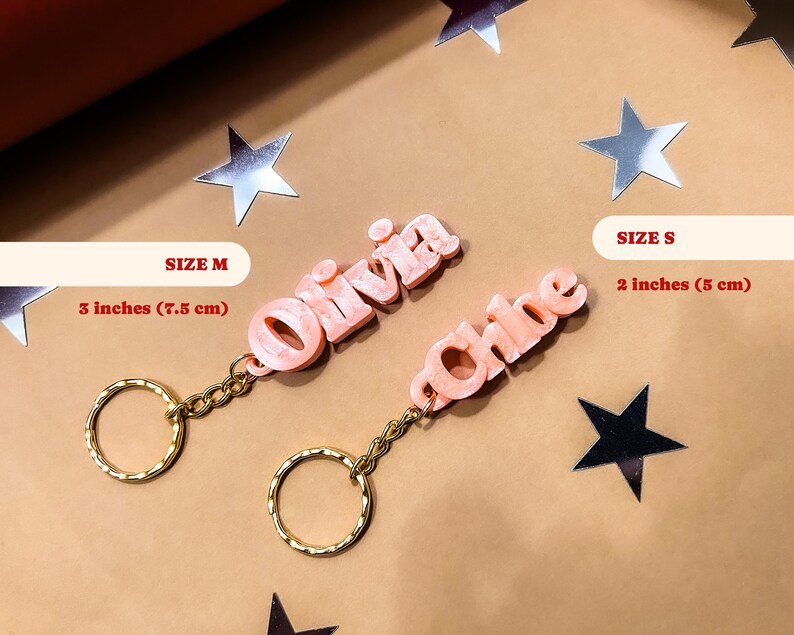 May include: Two pink personalized keychains with the names Olivia and Chloe. The Olivia keychain is 3 inches (7.5 cm) and the Chloe keychain is 2 inches (5 cm).