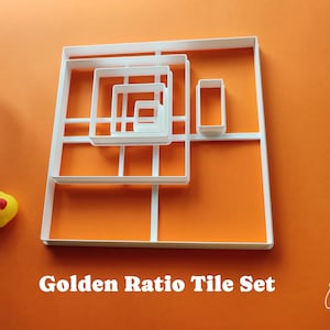 May include: A white Golden Ratio Tile Set on an orange background. The set includes various square and rectangular shapes, nested within each other. A small yellow rubber duck is in the lower left corner. The text "Golden Ratio Tile Set" is at the bottom.