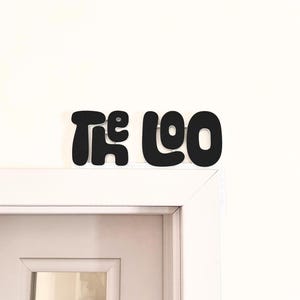以下が含まれることがあります： 白いドアの上に「The Loo」と書かれた黒い看板がある