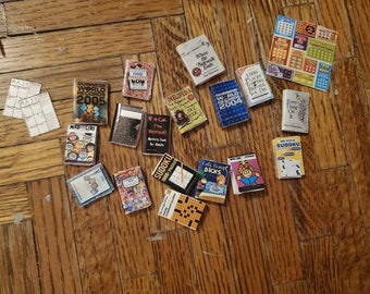 May include: A collection of miniature books with various titles, including "Guinness World Records 2005", "Mad Libs", "Find Now", "F*ck I'm Bored", "Jokelopedia", "Where the Sidewalk Ends", "World Records 2004", "1,000 Places to See Before You Die", "Every Thing On It", "Sudoku 1000-Puzzles", "Cats Being Dicks", "Sudoku", and "Win All".