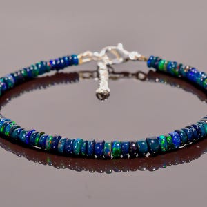 Peut inclure: Un bracelet de perles composé de petites perles rondes d'opale bleu foncé avec des éclairs d'iridescence verte et bleue. Le bracelet est monté sur une chaîne argentée avec un fermoir.