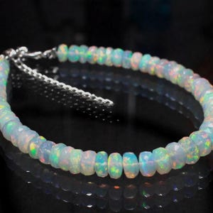 May include: A delicate bracelet made with iridescent white opal beads. The bracelet has a silver clasp and is approximately 7 inches in length.