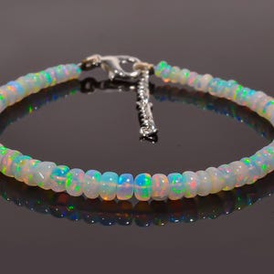 Peut inclure: Un bracelet en perles d'opale blanche avec un fermoir argenté. Les perles sont irisées et présentent un reflet arc-en-ciel.