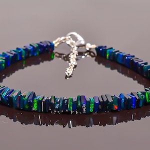 Puede incluir: Un collar de cadena de plata con una fila de cuentas rectangulares de ópalo azul oscuro, verde y negro.