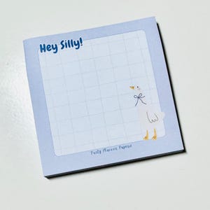 May include: A blue notepad with a grid pattern and the text "Hey Silly!" printed on the top. A white goose with a blue bow is illustrated on the bottom right corner. The notepad is labeled "Party Manner Paperie" at the bottom.