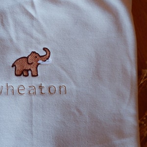 May include: A white sweatshirt with a brown embroidered elephant and the word "wheaton" in brown embroidery.