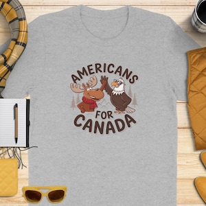 May include: A gray t-shirt with a cartoon moose and eagle high-fiving. The text "Americans for Canada" is printed on the shirt.