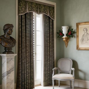 May include: An interior shot featuring a window with patterned curtains and a matching valance. A bronze bust sits atop a marble pedestal. A framed portrait and a decorative wall sconce with a vase and holly complete the elegant room.
