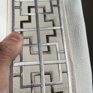 Puede incluir: Borde de tela beige con un patr&oacute;n geom&eacute;trico plateado y marr&oacute;n. El patr&oacute;n es un dise&ntilde;o repetitivo de cuadrados y rect&aacute;ngulos.