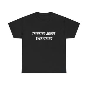 Peut inclure: T-shirt noir avec l'inscription blanche "THINKING ABOUT EVERYTHING" en caractères gras sans empattement. Le t-shirt a un col rond et des manches courtes. Le texte est centré sur la poitrine.