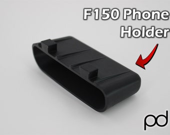 May include: Black plastic phone holder for a car. The holder has a rectangular shape with a rounded opening and a textured surface. The text "F150 Phone Holder" is visible in the image.