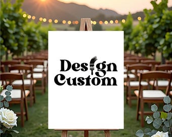 May include: A white sign on a wooden easel with the words "Design Custom" in black script. The sign is set up outdoors with rows of chairs, greenery, and a sunset in the background. White roses and greenery are in the foreground.