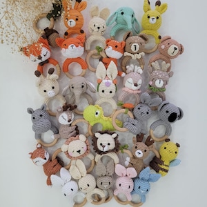 Könnte beinhalten: Eine Sammlung von gehäkelten Tier-Beißringen mit Holzringen. Die Beißringe sind in verschiedenen Farben und zeigen Tiere wie Füchse, Giraffen, Eulen und Hirsche.