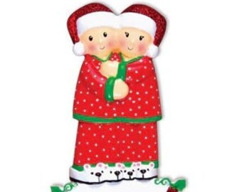 May include: Personalised Christmas bauble featuring a couple in red pyjamas with white polka dots and white bear slippers. The bauble has a blank banner for adding a name.