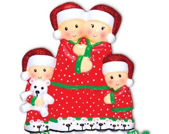May include: A Christmas bauble featuring a family of four wearing red and green pyjamas with white polka dots. The parents are holding hands and the children are holding cuddly toys. The bauble has a blank space for personalisation.