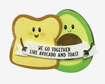 May include: A green avocado and a yellow piece of toast with smiling faces. The avocado is holding the toast with its arms and a banner reads "We go together like avocado and toast".