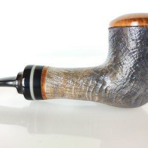 May include: A handcrafted tobacco pipe with a curved stem and a textured bowl. The pipe features a dark, almost black, bowl with a light brown wooden top. The stem is black with decorative bands of white, black, and brown.
