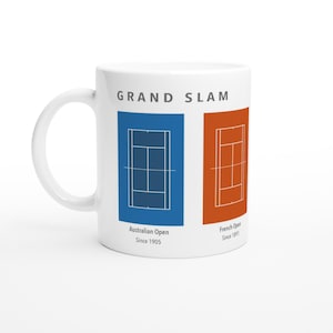 Puede incluir: Una taza de cerámica blanca con el texto GRAND SLAM en la parte superior. Debajo hay dos diagramas rectangulares de pistas de tenis: uno azul etiquetado Australian Open Since 1905 y uno naranja etiquetado French Open Since 1891 con líneas blancas.