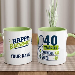 Puede incluir: Dos tazas de cerámica blanca con interior y asa de color verde claro. Una taza presenta el texto HAPPY BIRTHDAY! y YOUR NAME en azul y verde. La otra taza muestra una raqueta de tenis, una pelota de tenis y el texto 40 YEARS OLD EXPERIENCE: +10 SPEED: -10.