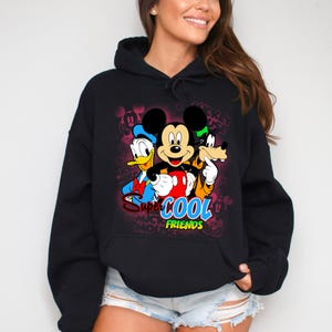 Puede incluir: Sudadera con capucha negra con un gr&aacute;fico colorido de Mickey Mouse, el Pato Donald y Goofy. El dise&ntilde;o incluye las palabras "Super Cool Friends". La sudadera tiene un bolsillo delantero y una capucha con cord&oacute;n.
