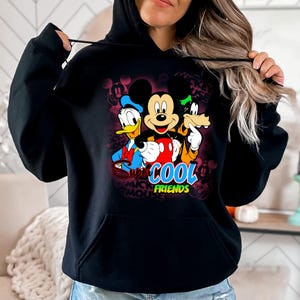 Puede incluir: Sudadera con capucha negra con un gr&aacute;fico colorido de Mickey Mouse, el Pato Donald y Goofy. El dise&ntilde;o incluye el texto "Super Cool Friends". La sudadera tiene un bolsillo delantero y una capucha con cord&oacute;n.