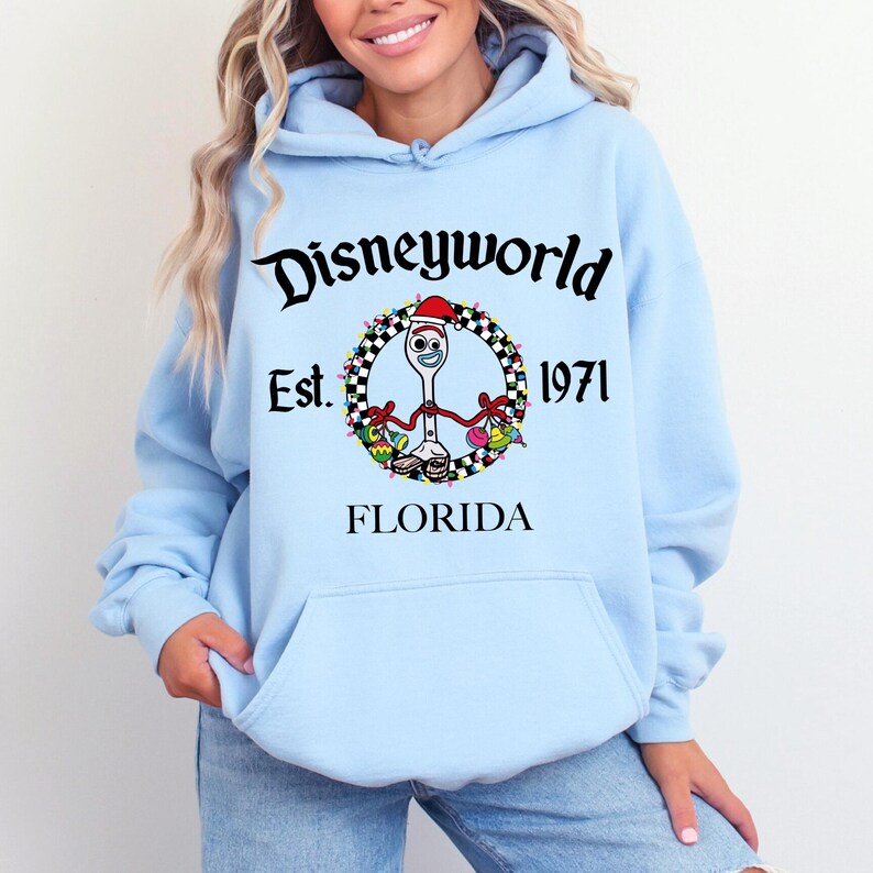 Pu&ograve; includere: Felpa con cappuccio azzurra con tasca frontale. Presenta una grafica di Forky di Toy Story con cappello da Babbo Natale, una ghirlanda e la scritta "Disneyworld Est. 1971 Florida".