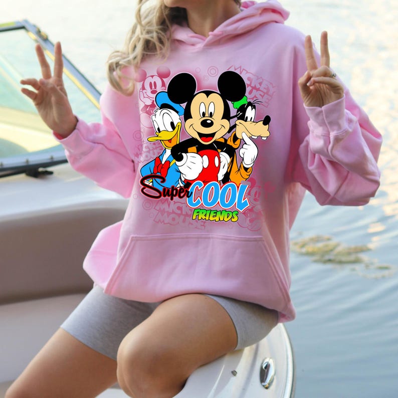 Puede incluir: Sudadera con capucha rosa claro con un dise&ntilde;o de Mickey Mouse, el Pato Donald y Goofy, con el texto "Super Cool Friends". El dise&ntilde;o est&aacute; centrado en la parte delantera de la sudadera.