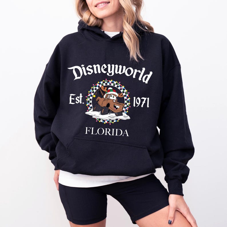 Pu&ograve; includere: Felpa con cappuccio nera con la scritta "Disneyworld" e un disegno di un'auto dei cartoni animati con un cappello di Babbo Natale. La felpa ha anche la scritta "Est. 1971" e "Florida" stampata.