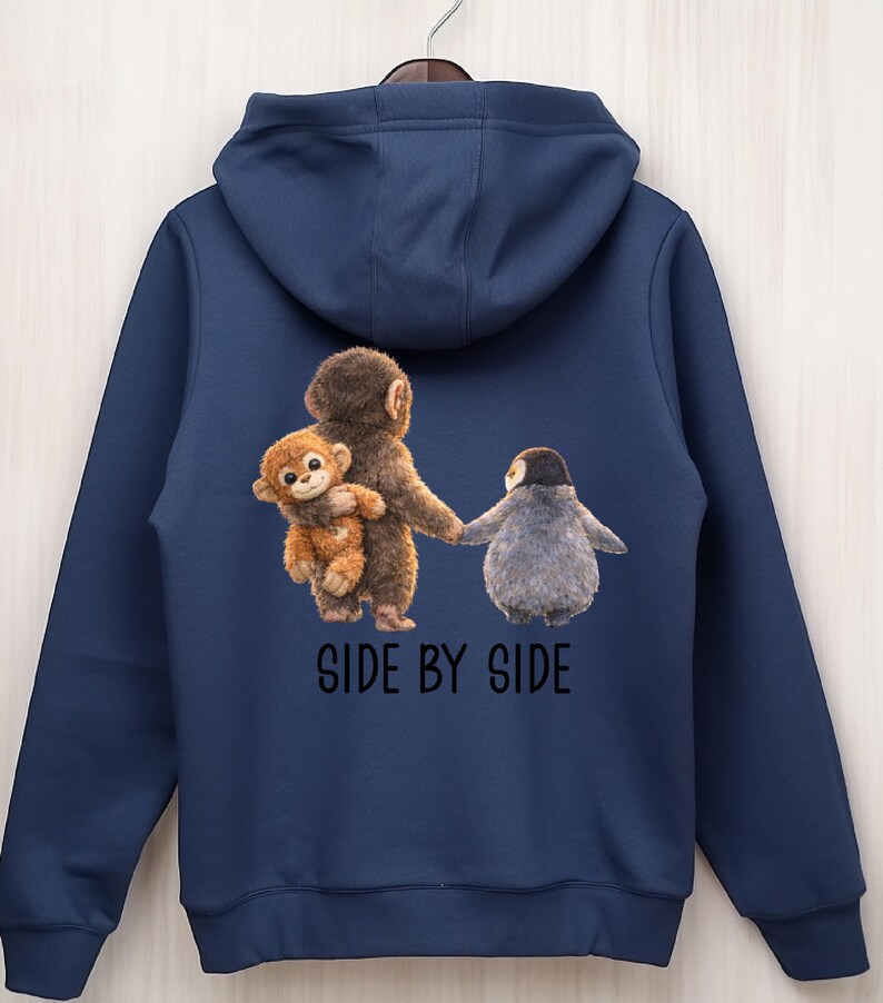 May include: Navy blue hoodie featuring a whimsical illustration of a monkey holding a smaller monkey, and a penguin holding hands. The phrase "SIDE BY SIDE" is printed below the image in black letters. The hoodie has a hood and a drawstring.