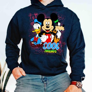 Puede incluir: Sudadera con capucha azul marino con Mickey Mouse, el Pato Donald y Goofy. El gr&aacute;fico incluye el texto "Super Cool Friends" en un dise&ntilde;o colorido. El fondo tiene un patr&oacute;n de siluetas de Mickey Mouse.