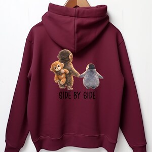 May include: A maroon hoodie with a hood and long sleeves. The back features a graphic of a monkey holding a smaller monkey and a penguin, with the text "SIDE BY SIDE" below the image.